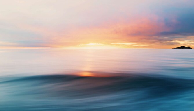 A sunset peeking between a cloudy sky and an ocean