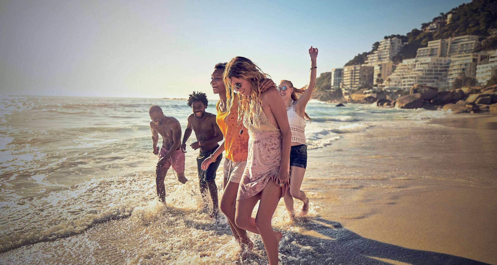 Lekfulla unga vänner som promenerar längs med solig havspromenad