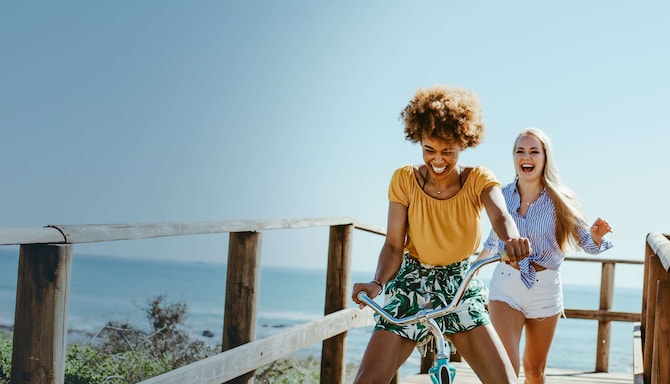 Two women on bikes laughing on a pier