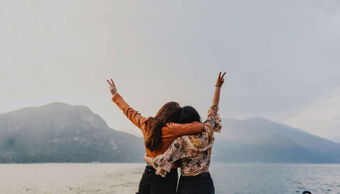 Two women, close together with one hand each in the air with peace sign