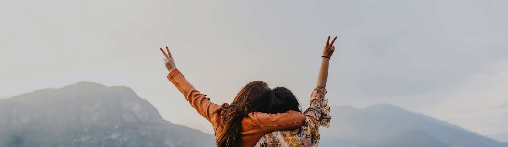 Two women, close together with one hand each in the air with peace sign