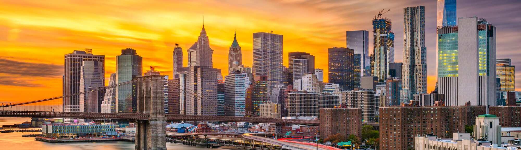 New York City at sunset with a view of the Brooklyn Bridge and NYC skyline.