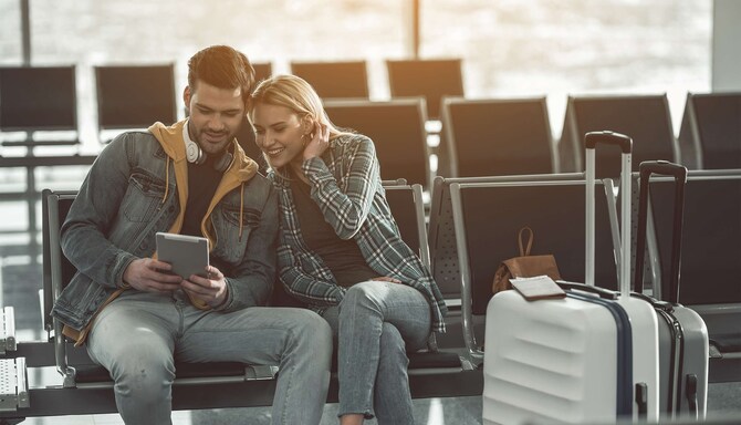 Couple sitting and waiting in airport, while looking at tablet device. oking at tablet device