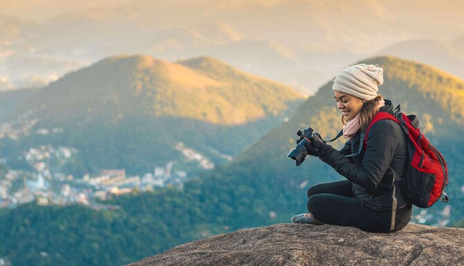 A woman sitting on a mountain while looking at her camera.