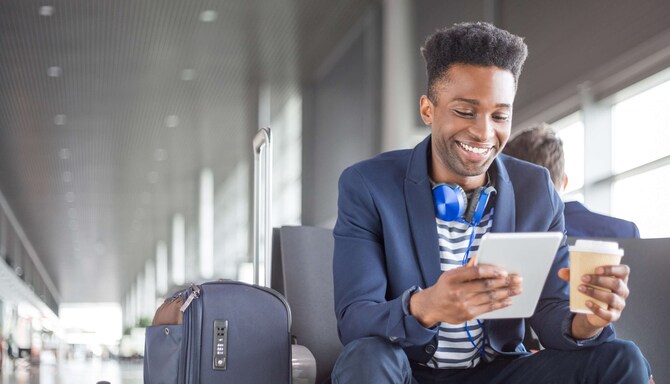 A young man waiting for a flight, looking at his tablet with a cup of coffee