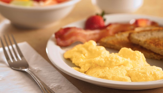 A plate of fluffy scrambled eggs, bacon and toast
