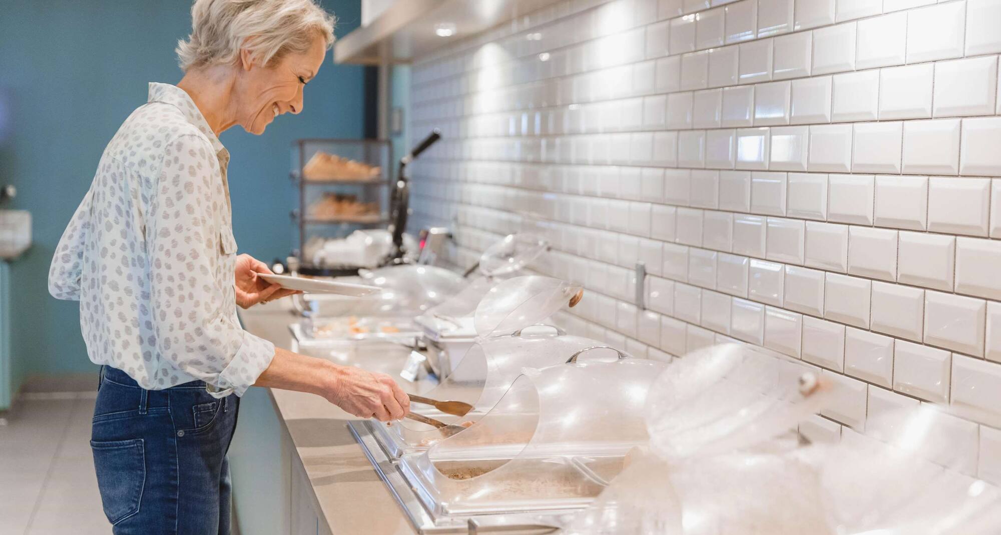Mujer de pie, sonriendo en el bufé, sosteniendo su plato