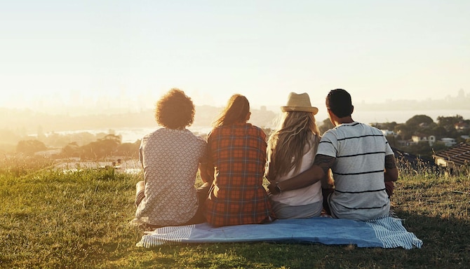 Ujęcie zza pleców czworga ludzi siedzących na kocu i oglądających miasteczko nad wodą