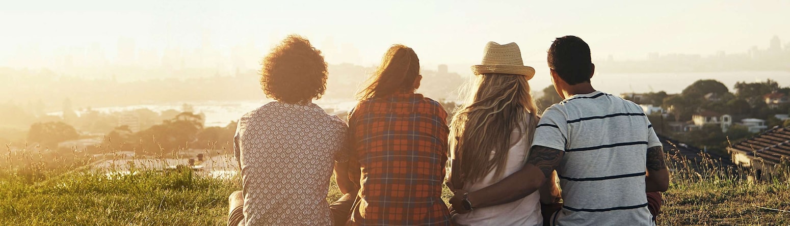 A view from the back of four people sitting on a blanket overlooking a town and water