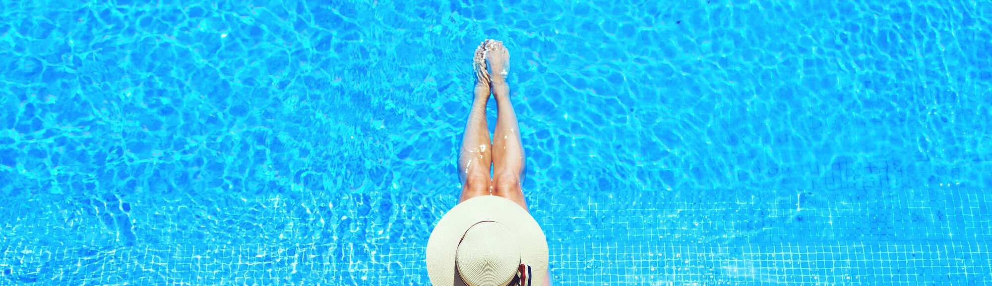 A woman in a large brimmed hat lounges in a pool