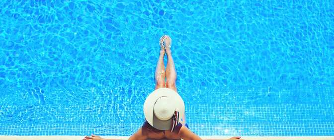 A woman in a large brimmed hat lounges in a pool