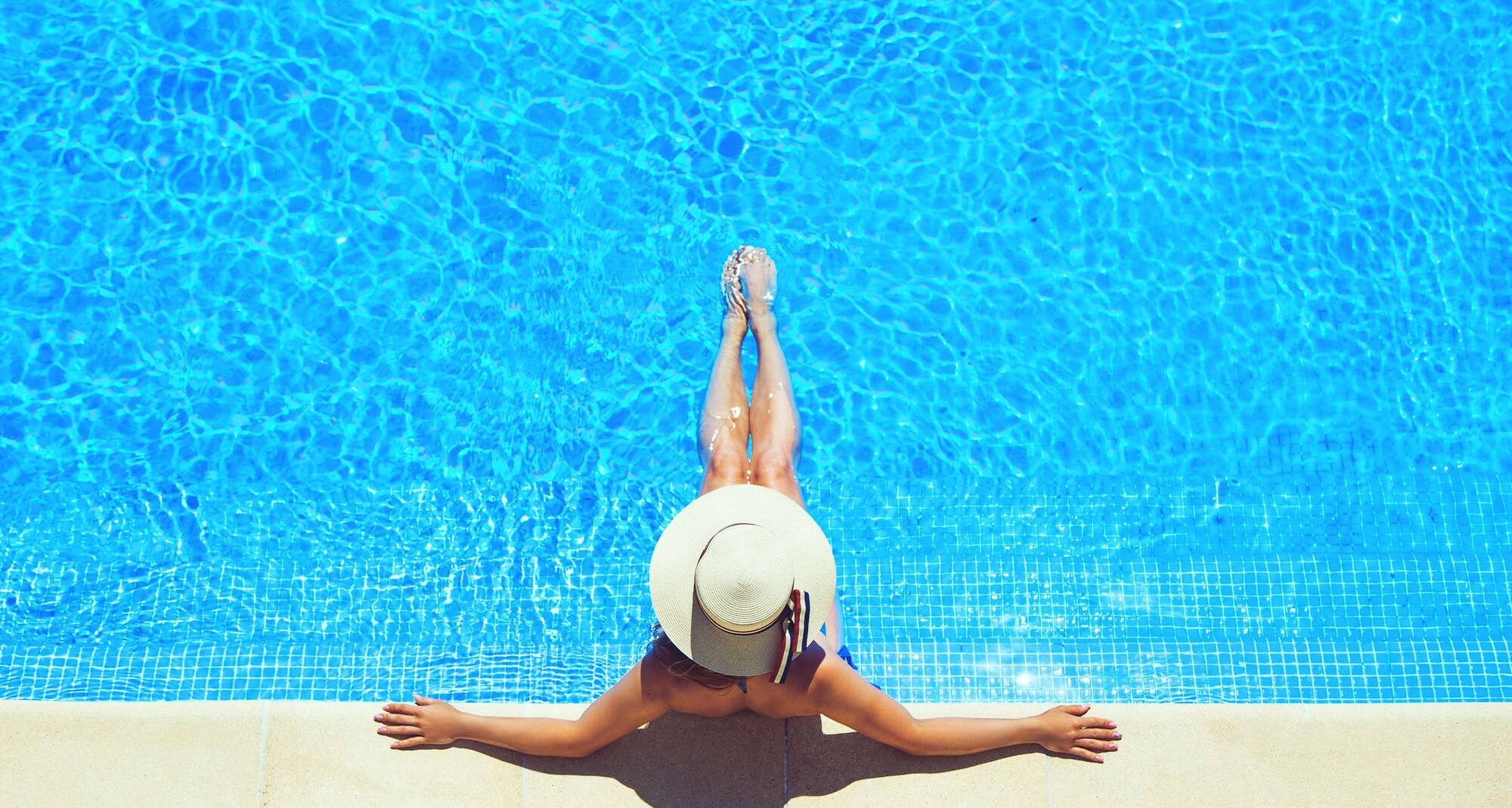 A woman in a large brimmed hat lounges in a pool