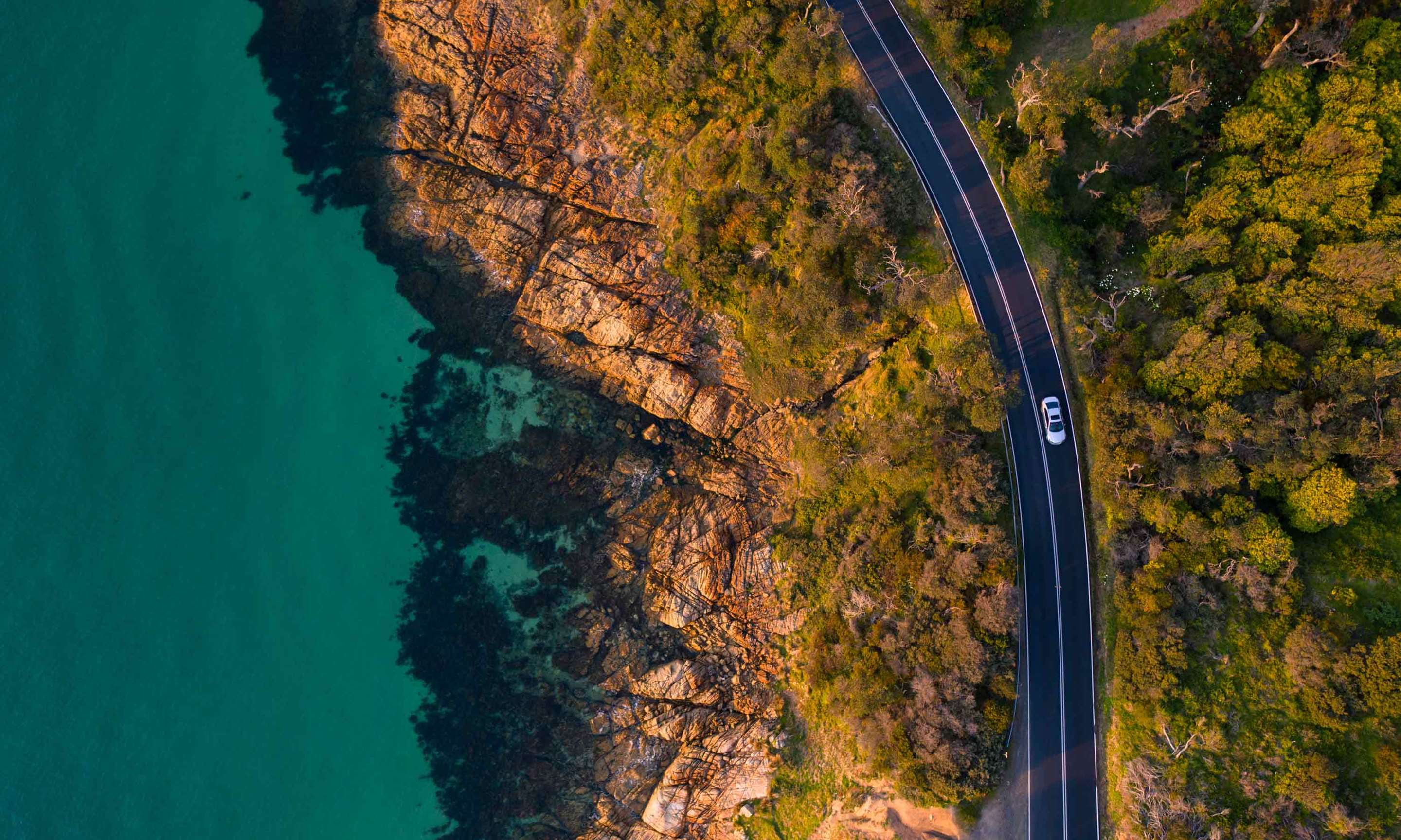 Aerial view of a car driving on road, along the waterfront.