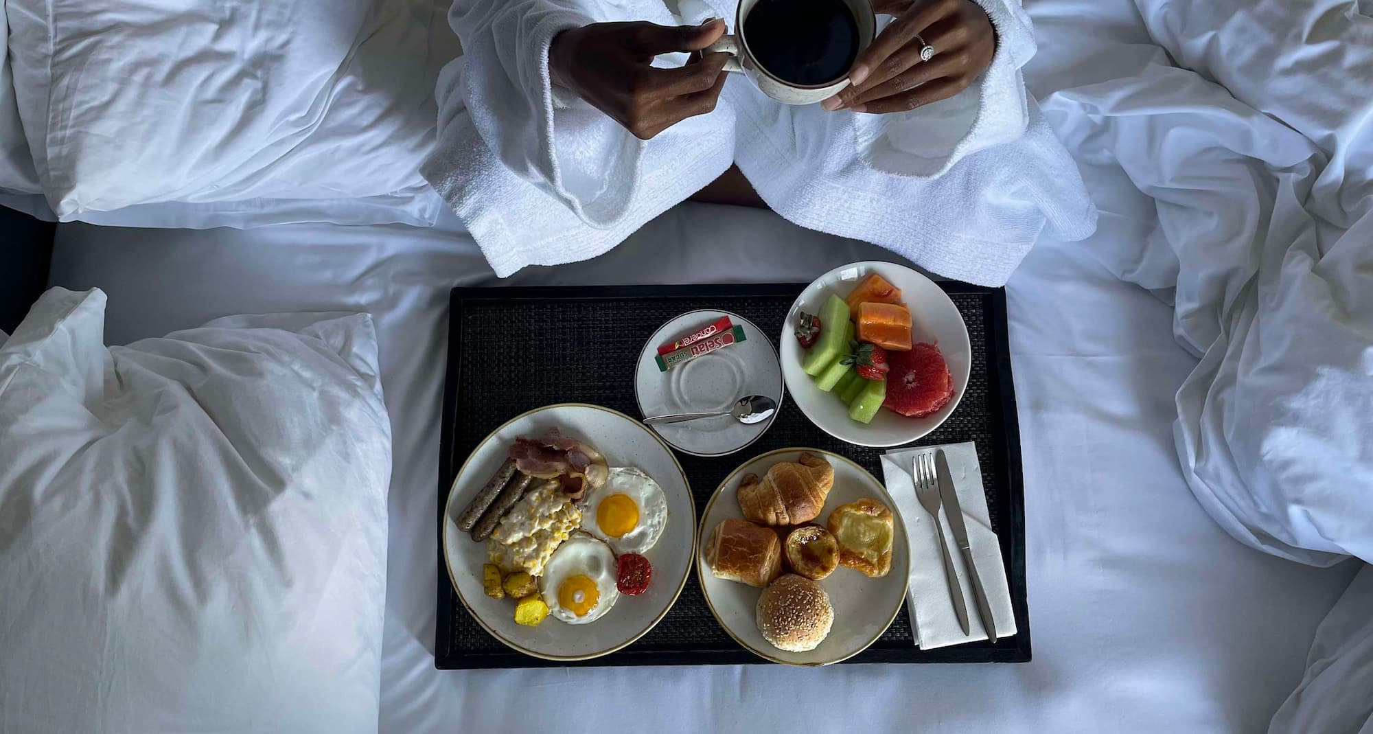 Woman holding a cup of coffee, enjoying breakfast on her bed.
