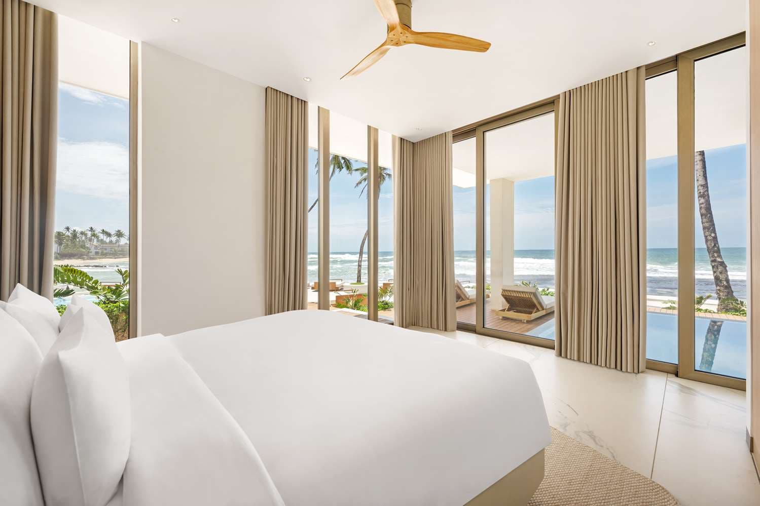 A suite bedroom with glass doors opening onto a private pool terrace and the beach.