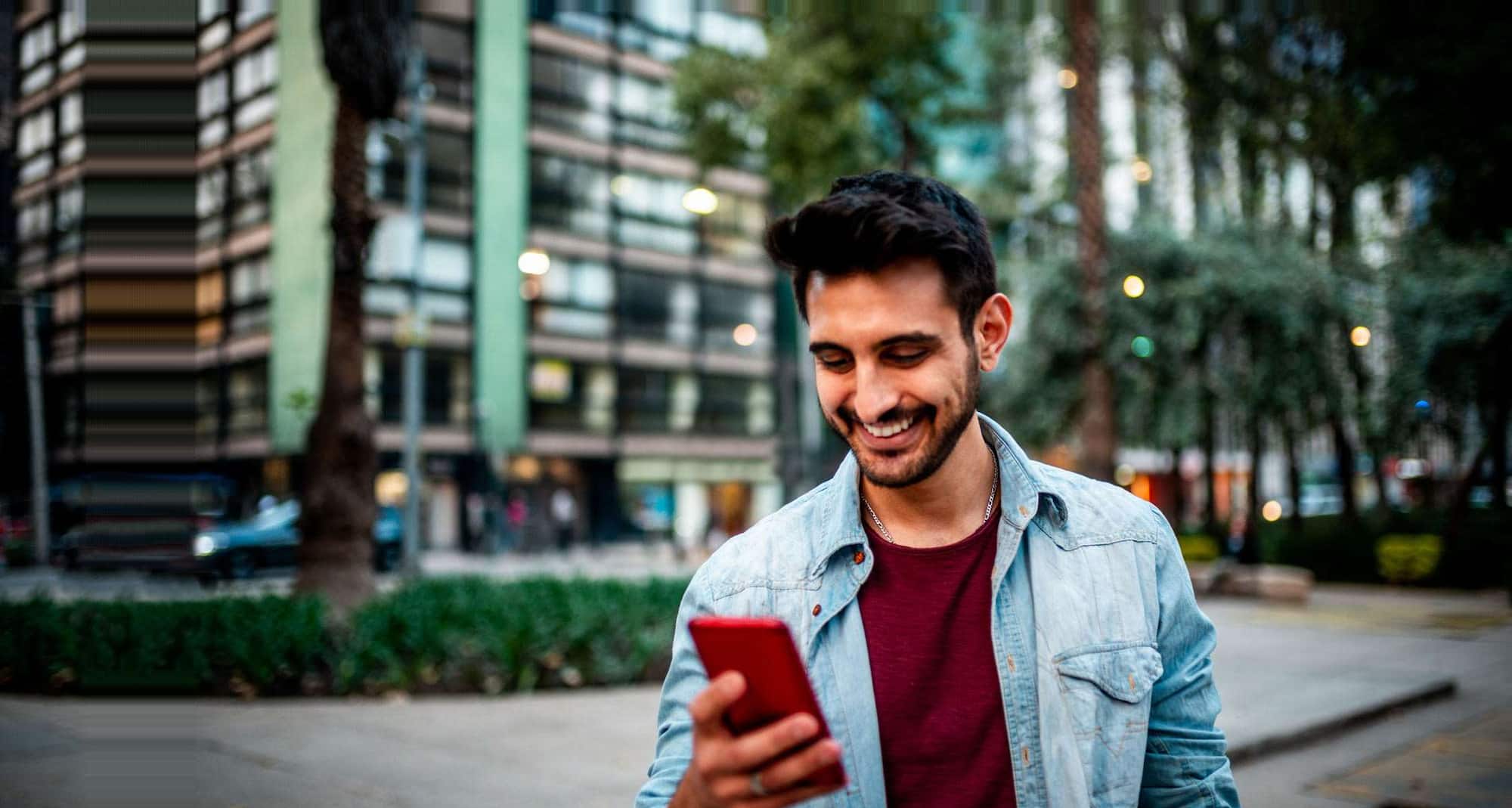 Şehir merkezinde meydanda cep telefonuna bakarak gülümseyen adam