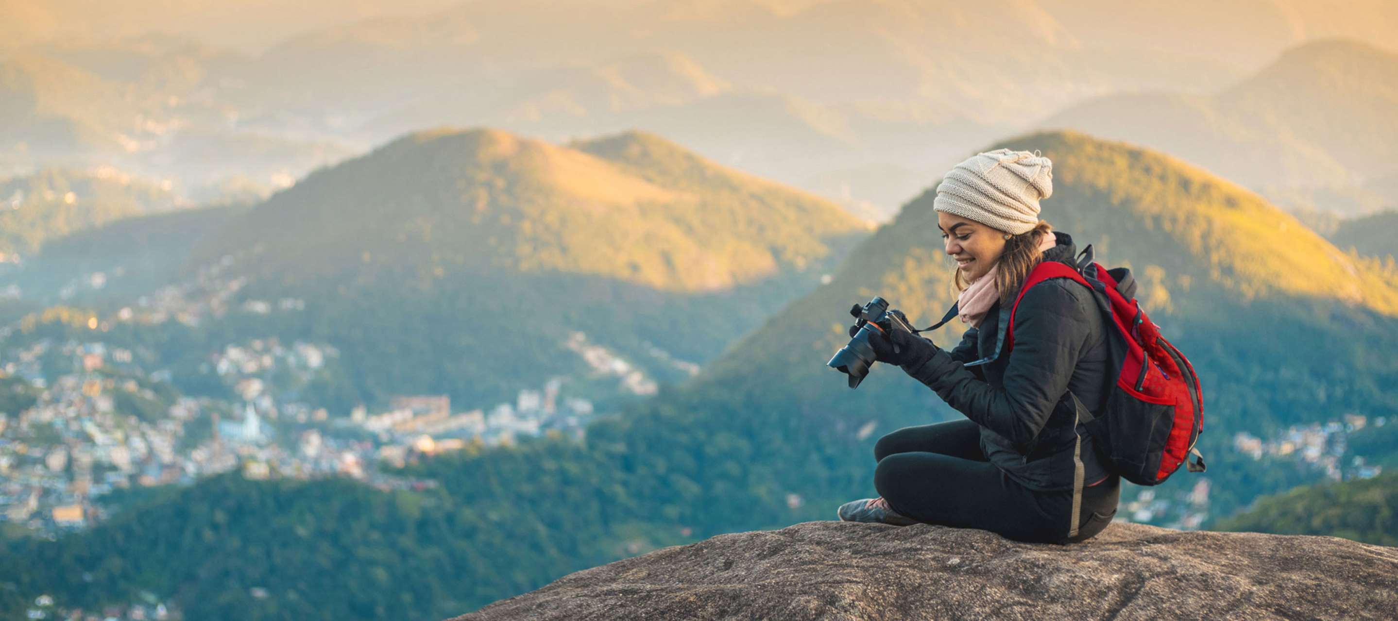 A woman sitting on a mountain while looking at her camera.