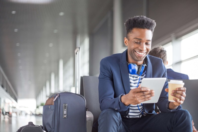 Un jeune homme attendant un vol, regardant sa tablette avec une tasse de café