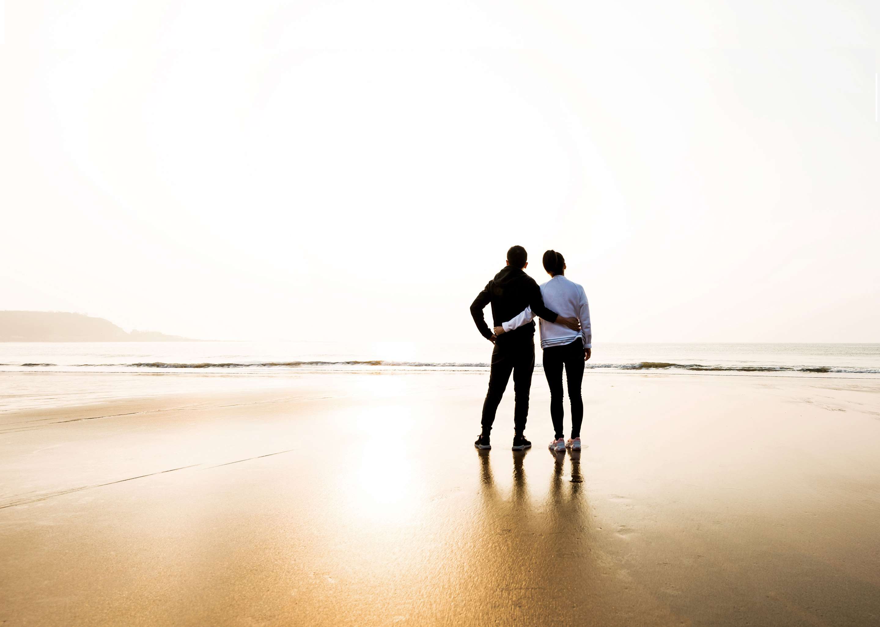 A couple standing arm in arm, on the beach.