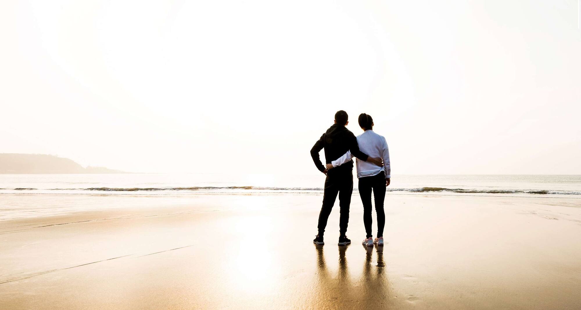 A couple standing arm in arm, on the beach.