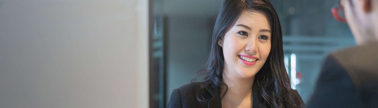 Smiling woman sitting across the table from a man at a meeting.