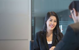 Smiling woman sitting across the table from a man at a meeting.