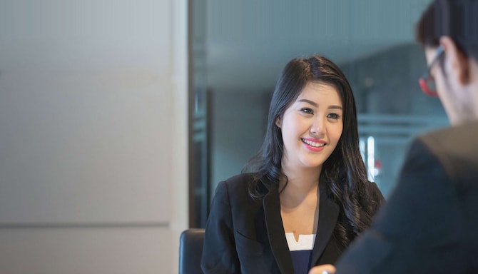 Smiling woman sitting across the table from a man at a meeting.
