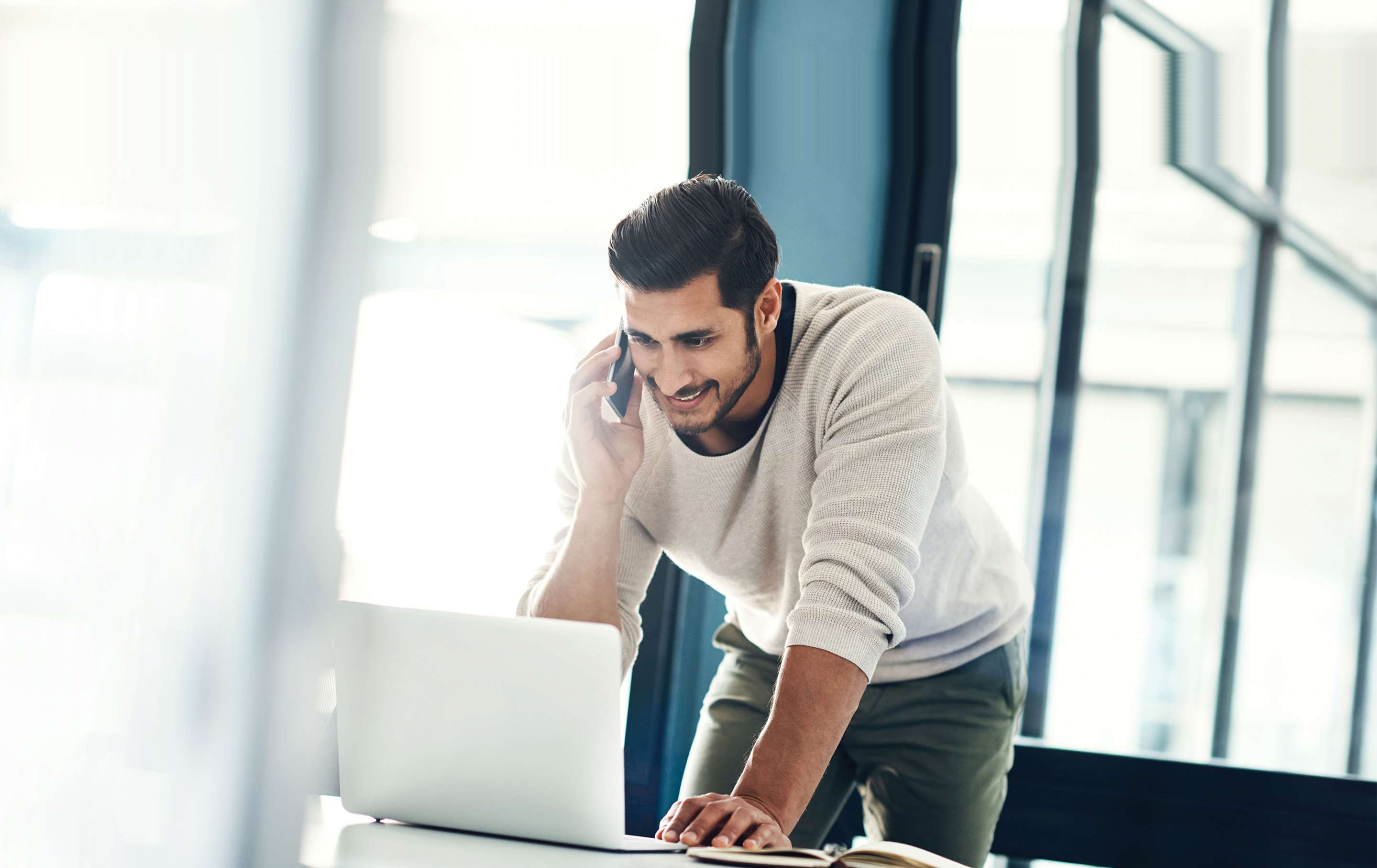 Business casual man talking on a cell phone while working on his laptop computer