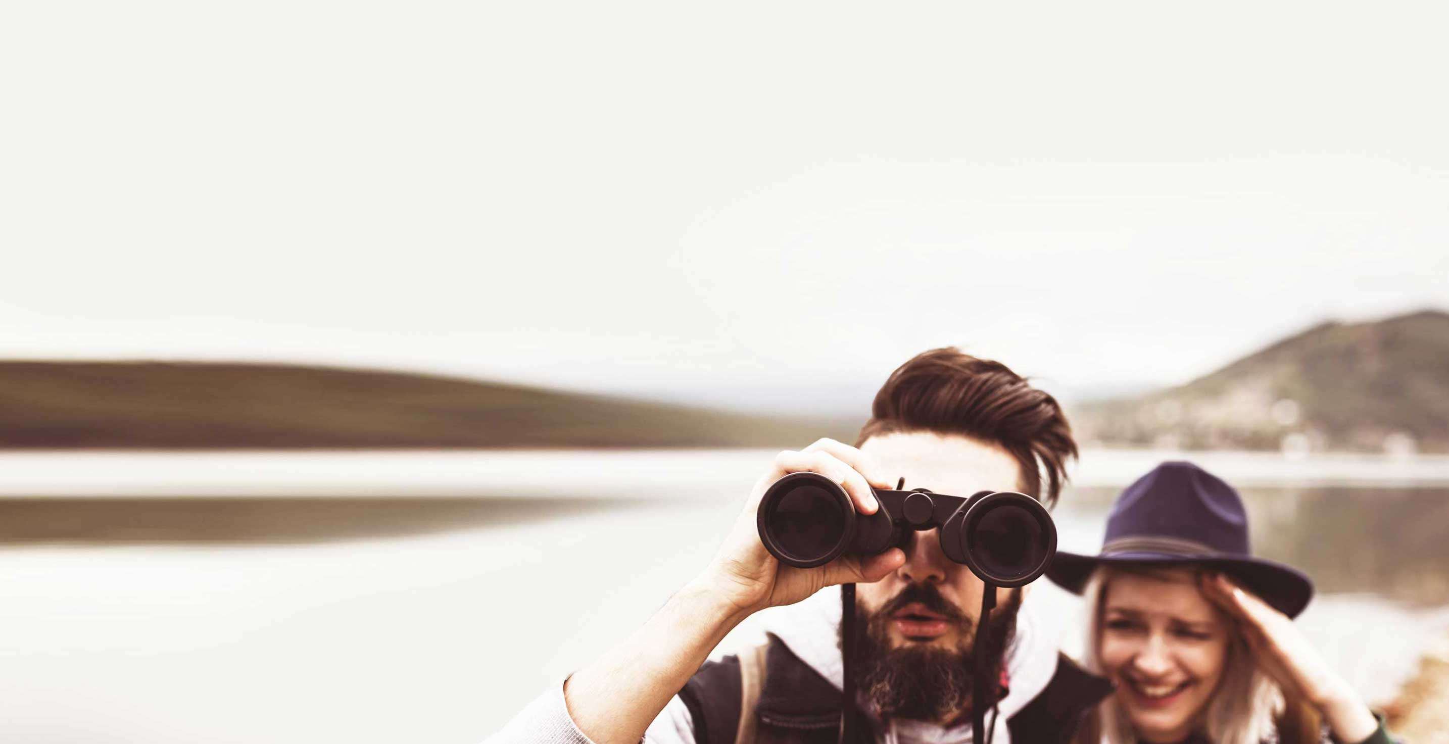 A man and woman, along the lake shore - he is looking through binoculars